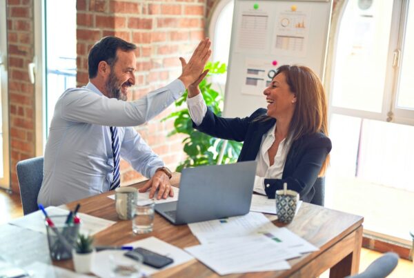 Franchise Broker Network Playbook: How Franchisors Recruit, Train, and Cut Brokers Without Channel Chaos 1 Franchise development partners celebrating a successful meeting with a high five across an office desk